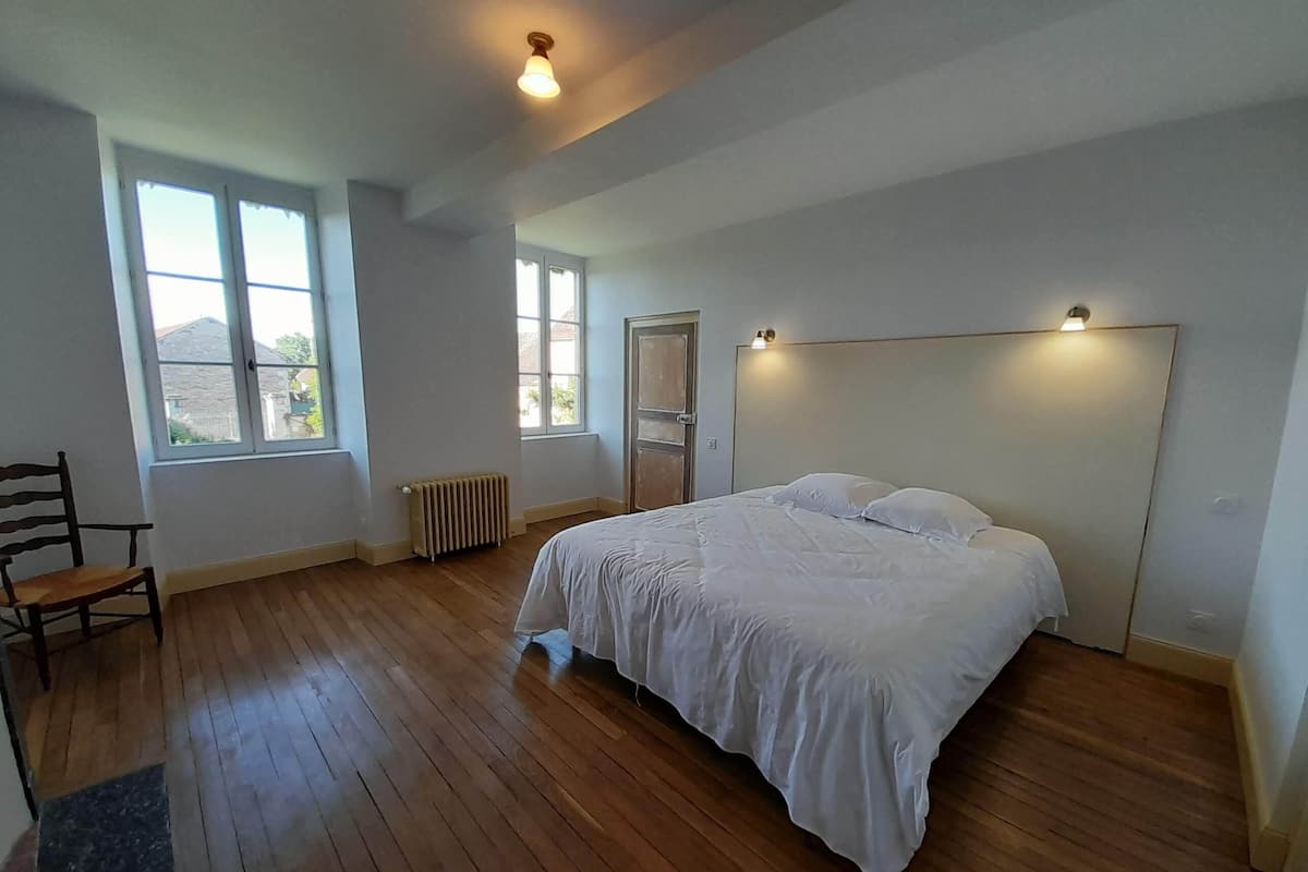 Quarto com uma cama grande, piso de madeira, um radiador e duas janelas.