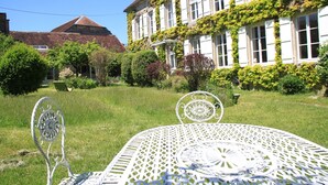 A white metal table and chair set in a garden with a building in the background. - Maravillon (Villon)