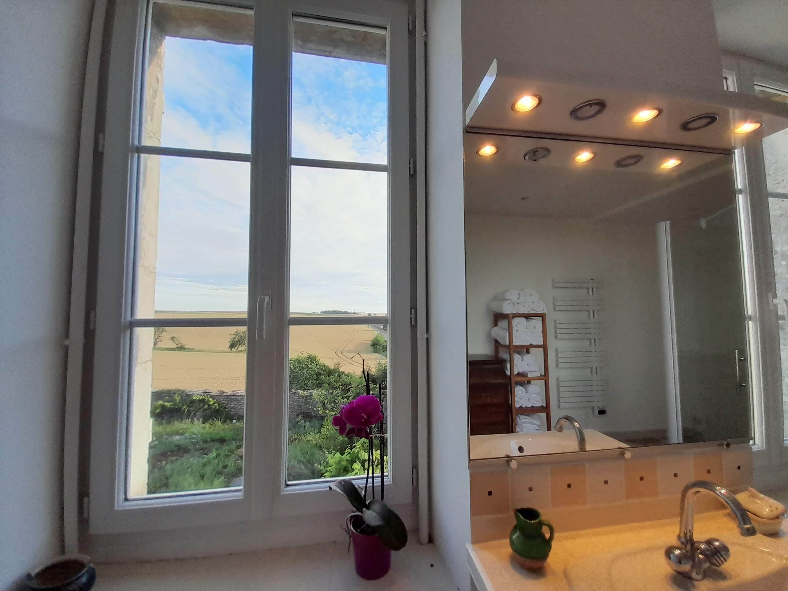 Ein Badezimmer mit großem Fenster, Waschbecken, Spiegel und Ablagefläche mit Handtüchern.