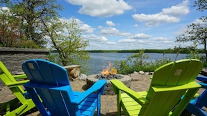 A lakeside patio with Adirondack chairs and a fire pit. - Morning Sun Cabin on Lake Metigoshe (Bottineau)