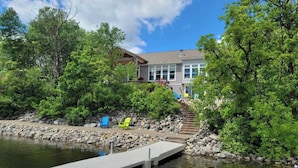 A lakeside property with a dock, a staircase leading to a house, and surrounding greenery. - Morning Sun Cabin on Lake Metigoshe (Bottineau)