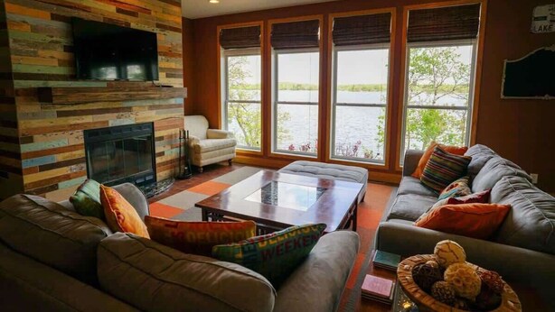 A cozy living room with a fireplace, large windows, and a comfortable seating area. - Morning Sun Cabin on Lake Metigoshe (Bottineau)