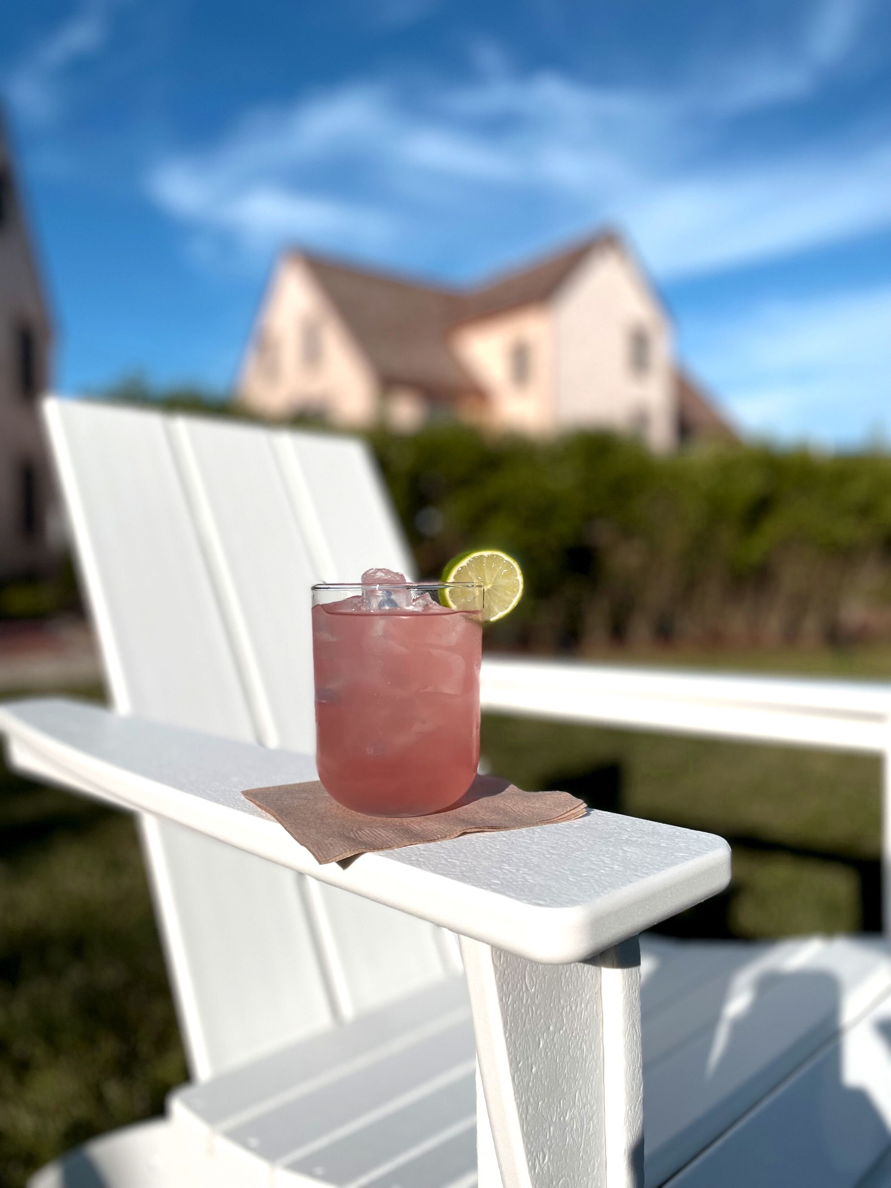 Un verre d’une boisson rouge, avec une tranche de citron vert, posé sur une chaise blanche à l’extérieur.