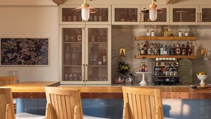 Een bar met houten stoelen, een koffieapparaat en flessen op planken.