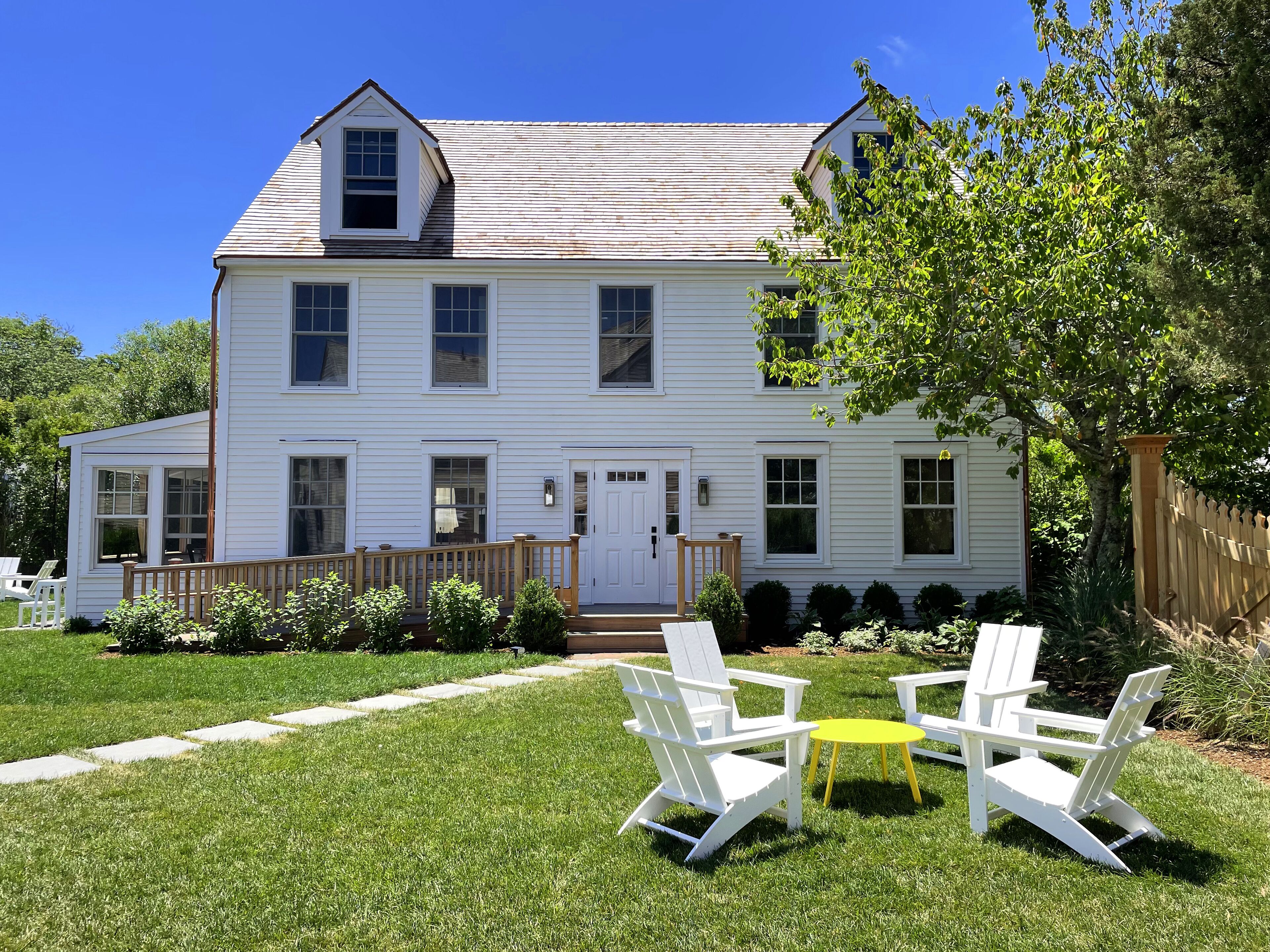 A two-story white house with a front porch, a small garden, and outdoor seating.
