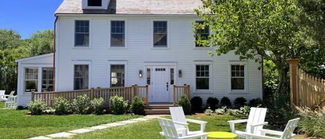 A two-story white house with a front porch, a small garden, and outdoor seating.
