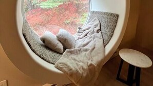 A cozy room with a circular window overlooking a forest.
