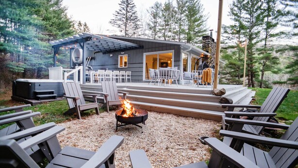 A cozy outdoor seating area with Adirondack chairs, a fire pit, and a stone fireplace.
