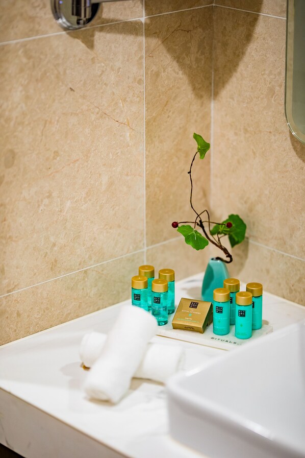Un baño con baldosas color beige, un lavamanos blanco y una pequeña planta.