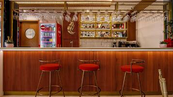 Un espace bar avec un comptoir en bois, trois tabourets de bar rouges et un réfrigérateur Coca-Cola.