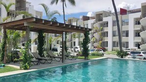 Et poolområde med liggestole, en pergola og udsigt til moderne bygninger.