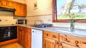 A kitchen with wooden cabinets, a microwave, a dishwasher, and a window with a view of a tree and a house. - Ta Mill Brookview Lodge 2 (Launceston)