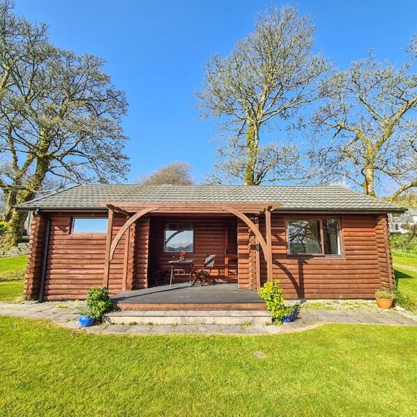 A small, rustic log cabin with a porch and a table and chairs set outside. - Ta Mill Brookview Lodge 2 (Launceston)