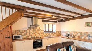 A kitchen with a brown leather sofa, a microwave, and a tiled backsplash. - Ta Mill Millers Cottage in a Stunning Retreat (Launceston)