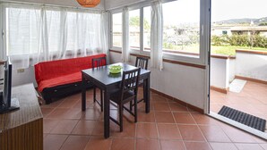 A room with a dining table and chairs, a red sofa, and a window with curtains. - CASA GINESTRA - GINESTRA 2 (Campo nell'Elba)