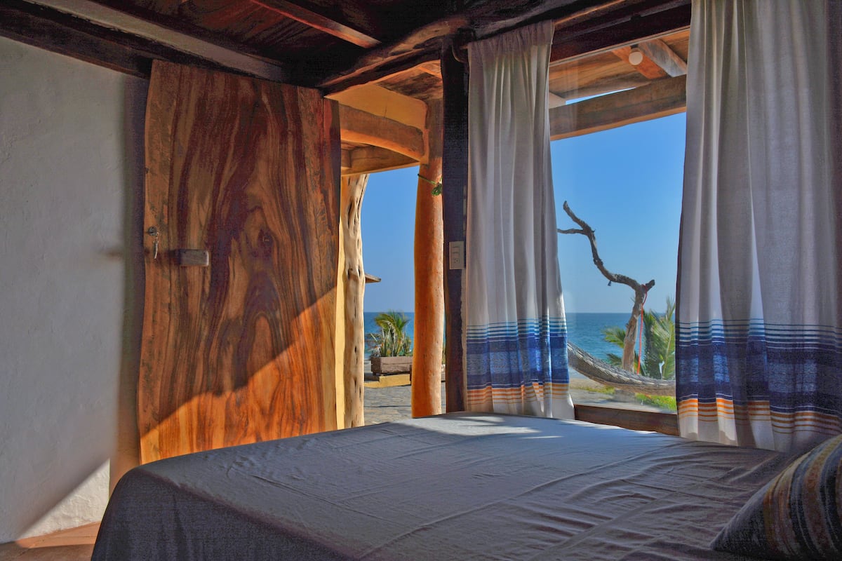 Une chambre avec un grand lit, une porte en bois et une vue sur la plage et l’océan.