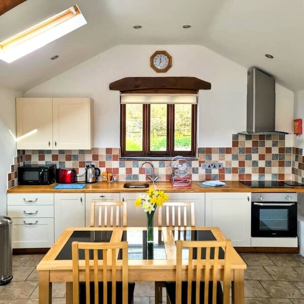 Une cuisine avec une table à manger, des chaises, une horloge, une fenêtre et une cuisinière.