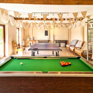 Enjoy a game of pool in this cozy room with a billiard table, chairs, and a cue.