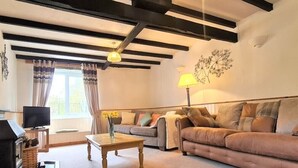 A living room with a sofa, a coffee table, a TV, and a fireplace. - Ta Mill Forge Cottage in a Stunning Retreat (Launceston)