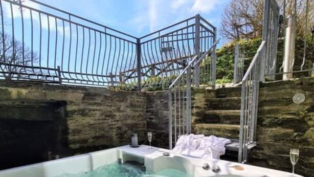 A hot tub with a stone wall backdrop, a metal railing, and a staircase leading to a higher level. - Ta Mill Forge Cottage in a Stunning Retreat (Launceston)