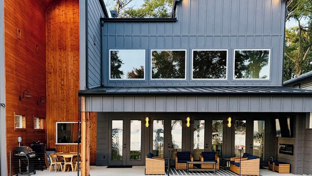 Een modern huis met twee verdiepingen, een ruime houten inrichting, een overdekt terras met zitplaatsen en een verzorgd gazon.