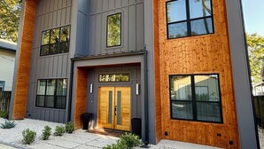 Een modern huis met twee verdiepingen, een symmetrische gevel, grote ramen en een houten accentmuur.