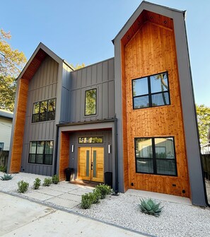 A modern two-story house with a symmetrical facade, large windows, and a wooden accent wall. - Luxury Lakefront - Huge Patio + Private Yard + Boat + Sleeps 14 (Mabank)