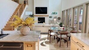 Een ruime woonkamer met een trap, een flatscreen-tv, een bank, een eettafel en een groot raam met uitzicht op de omgeving.