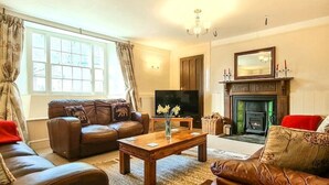 A living room with a fireplace, leather sofas, a coffee table, and a television. - Ta Mill House in a Stunning Retreat (Launceston)
