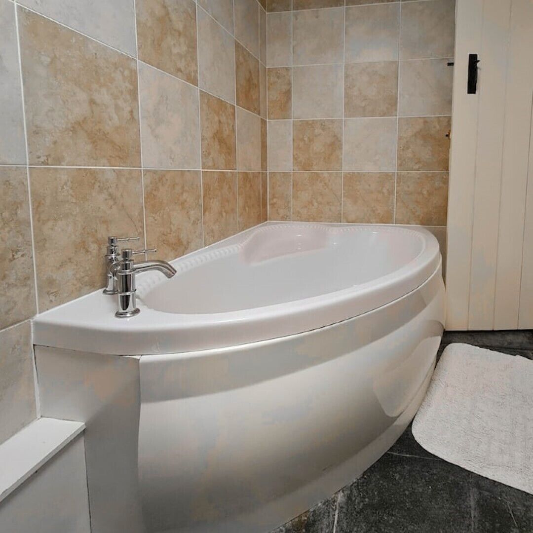 Et moderne badeværelse med et fristående badekar, et vægmonteret armatur og beige flisevægge.
