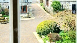 A stone building with a cobblestone street, a small garden with a neatly trimmed bush, and a visible window with a wooden frame. - Ta Mill House in a Stunning Retreat (Launceston)