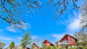 Una casa rossa con un balcone, circondata da un prato curato e alberi.