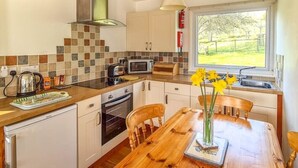 Una cucina moderna con un tavolo di legno, mobili bianchi e vista su un paesaggio verde.