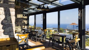 Un restaurant doté d’une terrasse, de murs en pierre et offrant une vue sur l’océan.