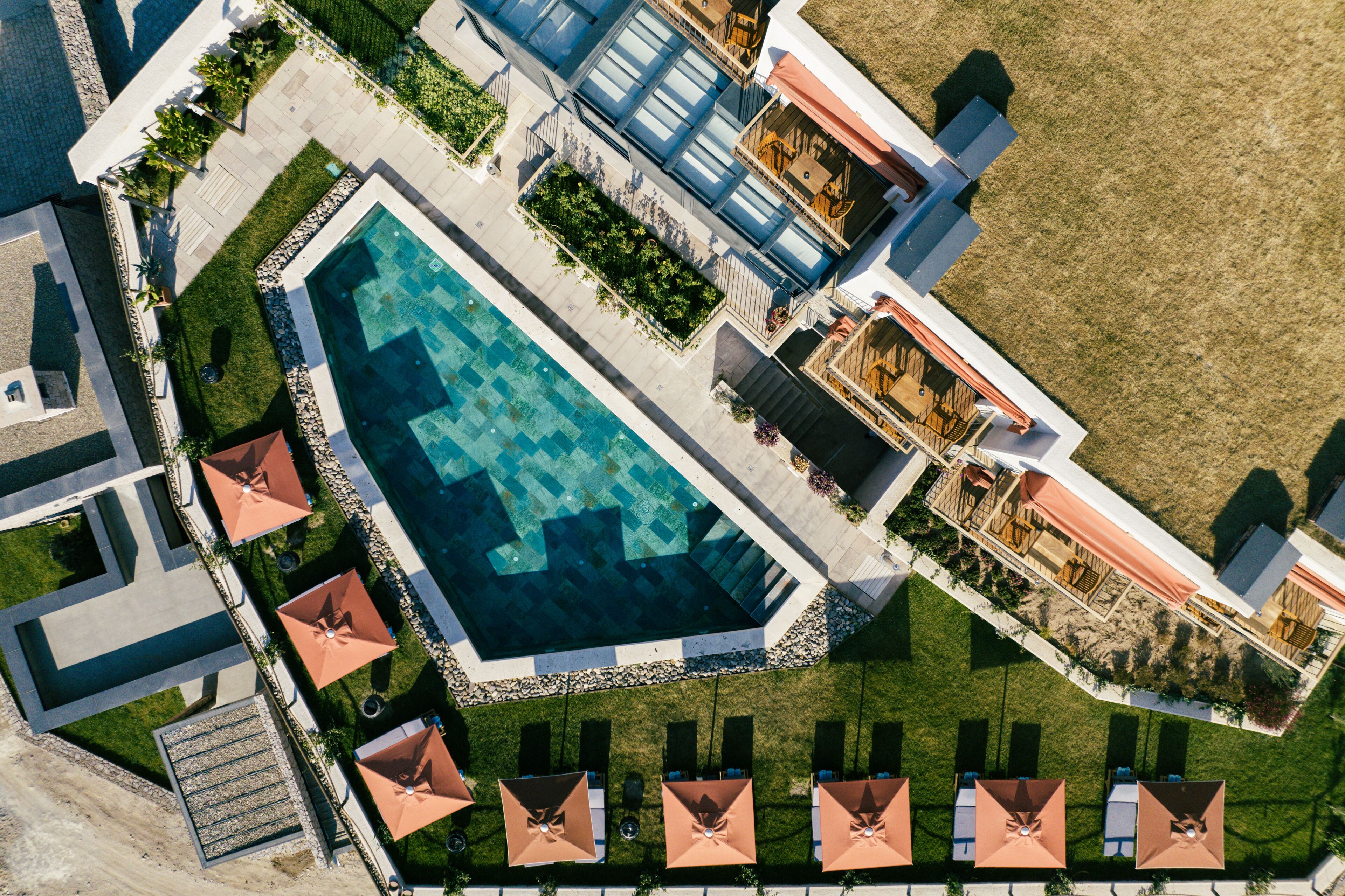 An aerial view of a resort with a large swimming pool, sun loungers, and a well-maintained lawn.