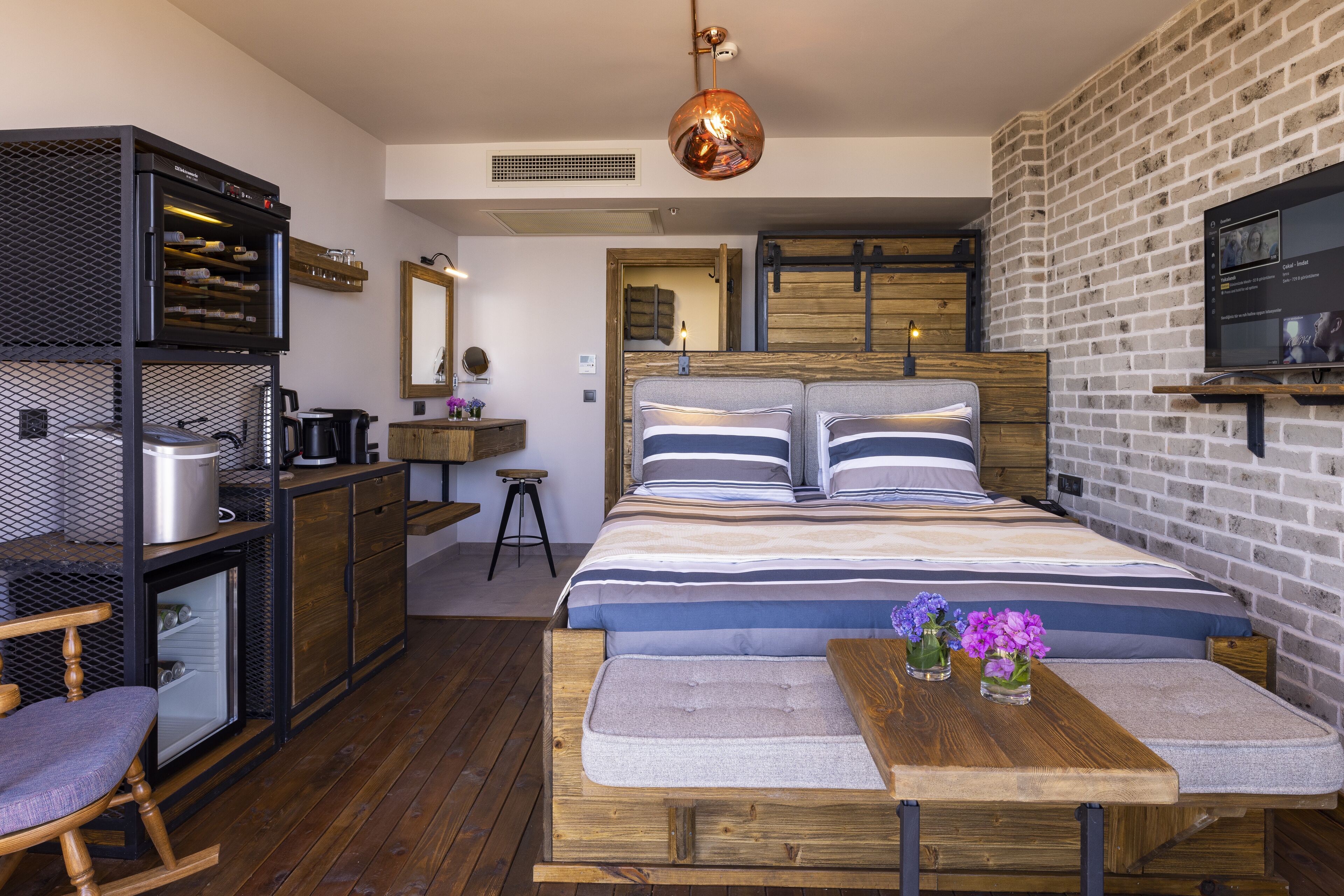 Een moderne slaapkamer met een groot bed, houten meubels, een kleine kitchenette en een metselwerk muur.