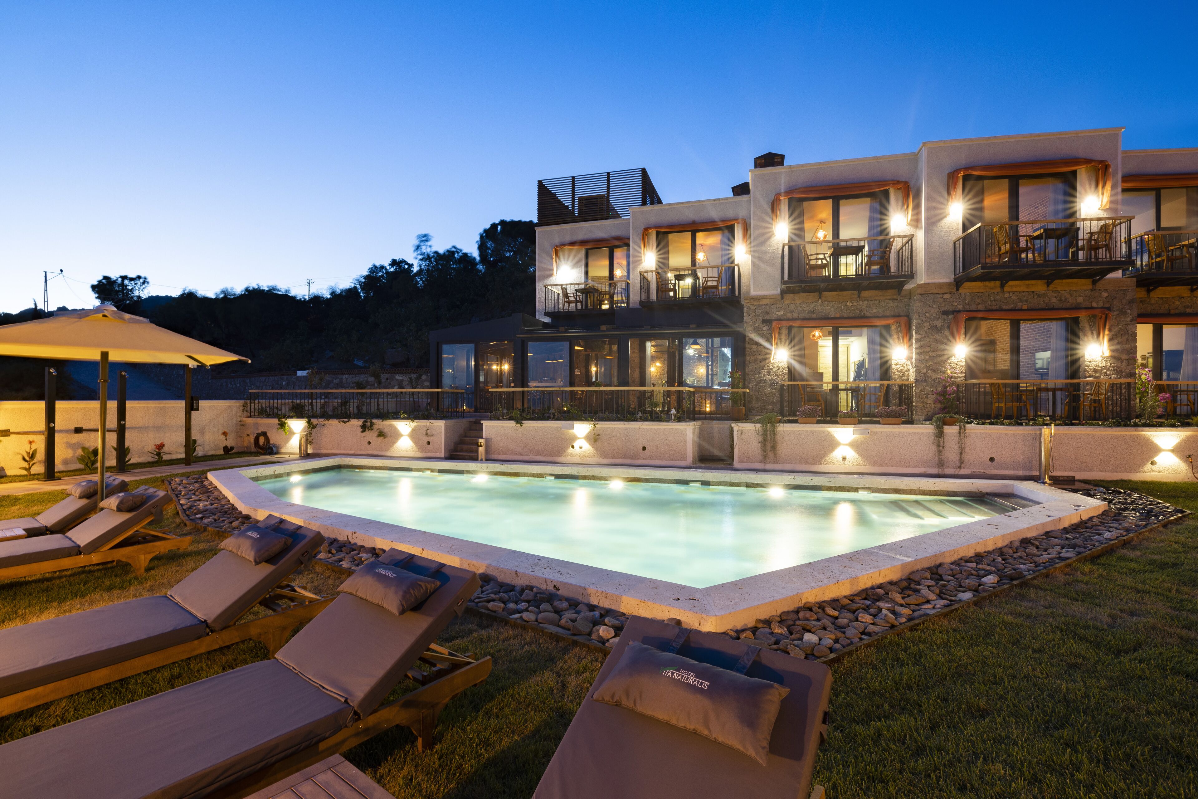 Un moderno edificio de varios pisos con piscina, sillones de exterior y un patio bien iluminado.