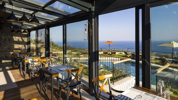Un espace repas avec des tables et des chaises, de grandes fenêtres et une vue sur la mer.