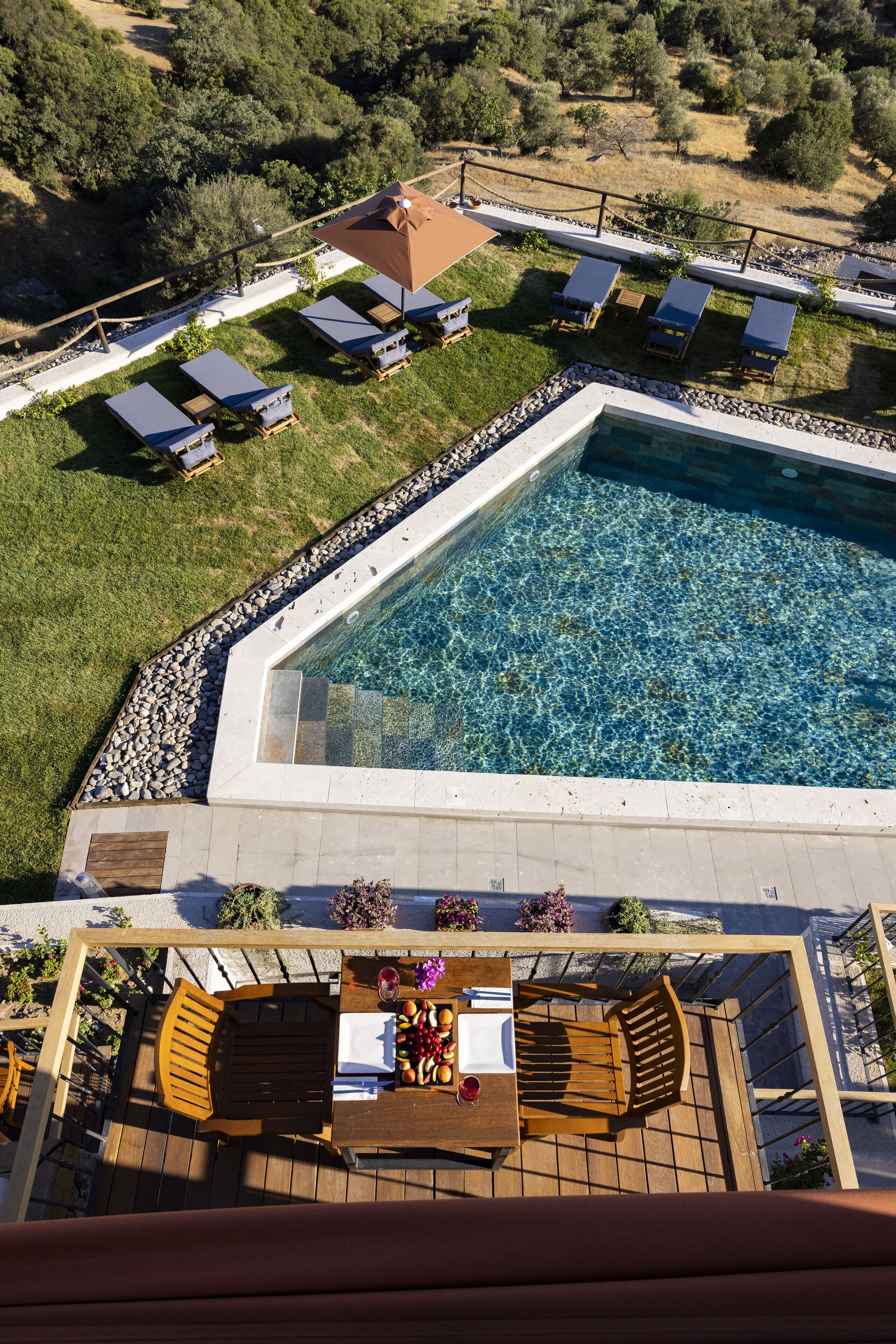 Vue aérienne d’un complexe hôtelier doté d’une piscine, de chaises longues et d’une terrasse aménagée avec des tables et des chaises.