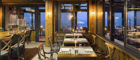 A restaurant with wooden interiors, large windows, and a view of the sea.