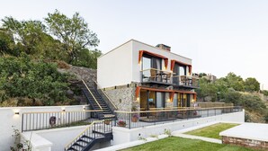 Une maison moderne à deux étages, dotée d’une façade en pierre, d’un balcon avec coin salon extérieur et d’un escalier menant à l’étage supérieur.