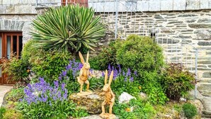 A stone building with a garden featuring sculptures and purple flowers. - Ta Mill Hayloft Cottage in a Stunning Retreat (Launceston)