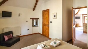 A bedroom with a bed, a wooden door, a radiator, a television, and a small window. - Ta Mill Hayloft Cottage in a Stunning Retreat (Launceston)