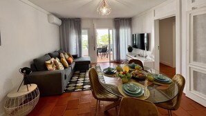 A modern living room with a dining area, a sofa with cushions, a round coffee table, and a TV mounted on the wall.
