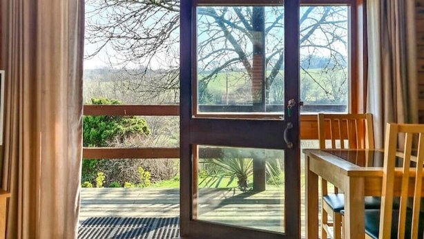 A wooden cabin with a large glass door leading to an outdoor area. - Cosy log-cabin style lodge with outdoor Lay-Z-Spa in rural, North Cornwall. (Launceston)