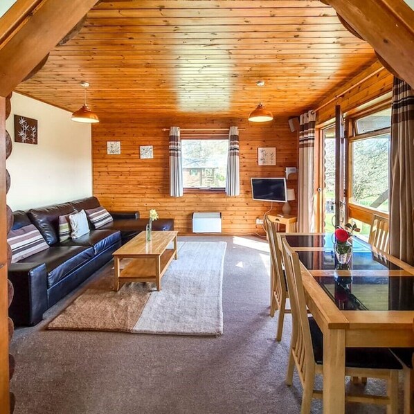 A cozy cabin interior with a wooden ceiling, a sofa, a dining table, and a TV. - Cosy log-cabin style lodge with outdoor Lay-Z-Spa in rural, North Cornwall. (Launceston)