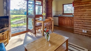 A cozy log cabin interior with a dining area, kitchen, and large windows offering a view of the outdoors.