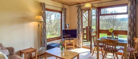 Un salon chaleureux avec un plafond en bois, un canapé, une table basse, un téléviseur et un coin repas comprenant une table et des chaises.