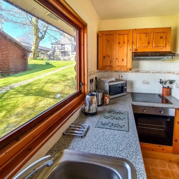 A kitchen with wooden cabinets, a microwave, a toaster, and a sink. - Cosy log-cabin style lodge with outdoor Lay-Z-Spa in rural, North Cornwall. (Launceston)