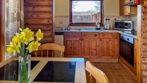 A wooden cabin interior with a kitchen area, a dining table with chairs, and a vase of yellow flowers.